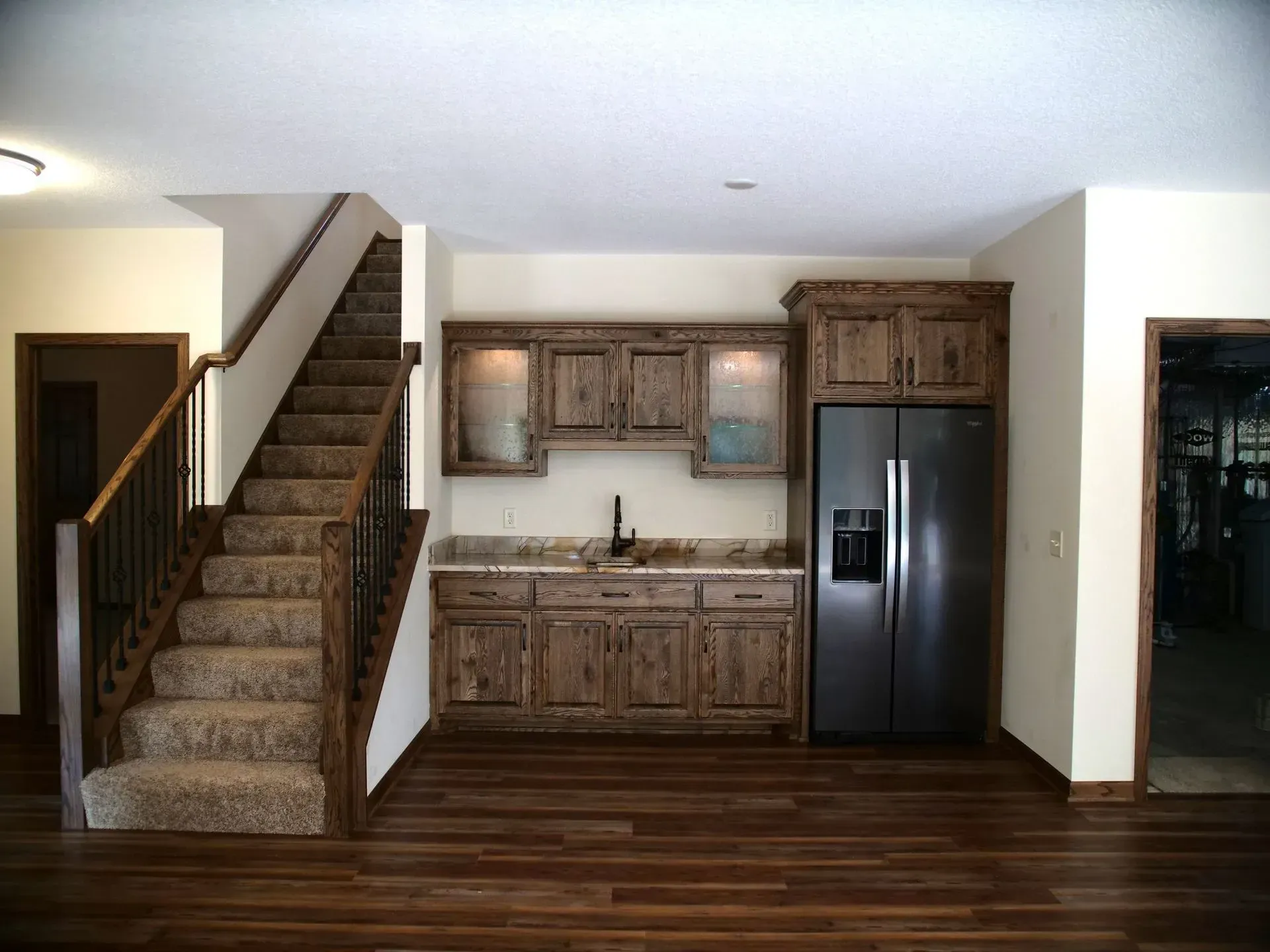 Interior with stairs, a mini-kitchen with rustic cabinets, and a stainless steel refrigerator.