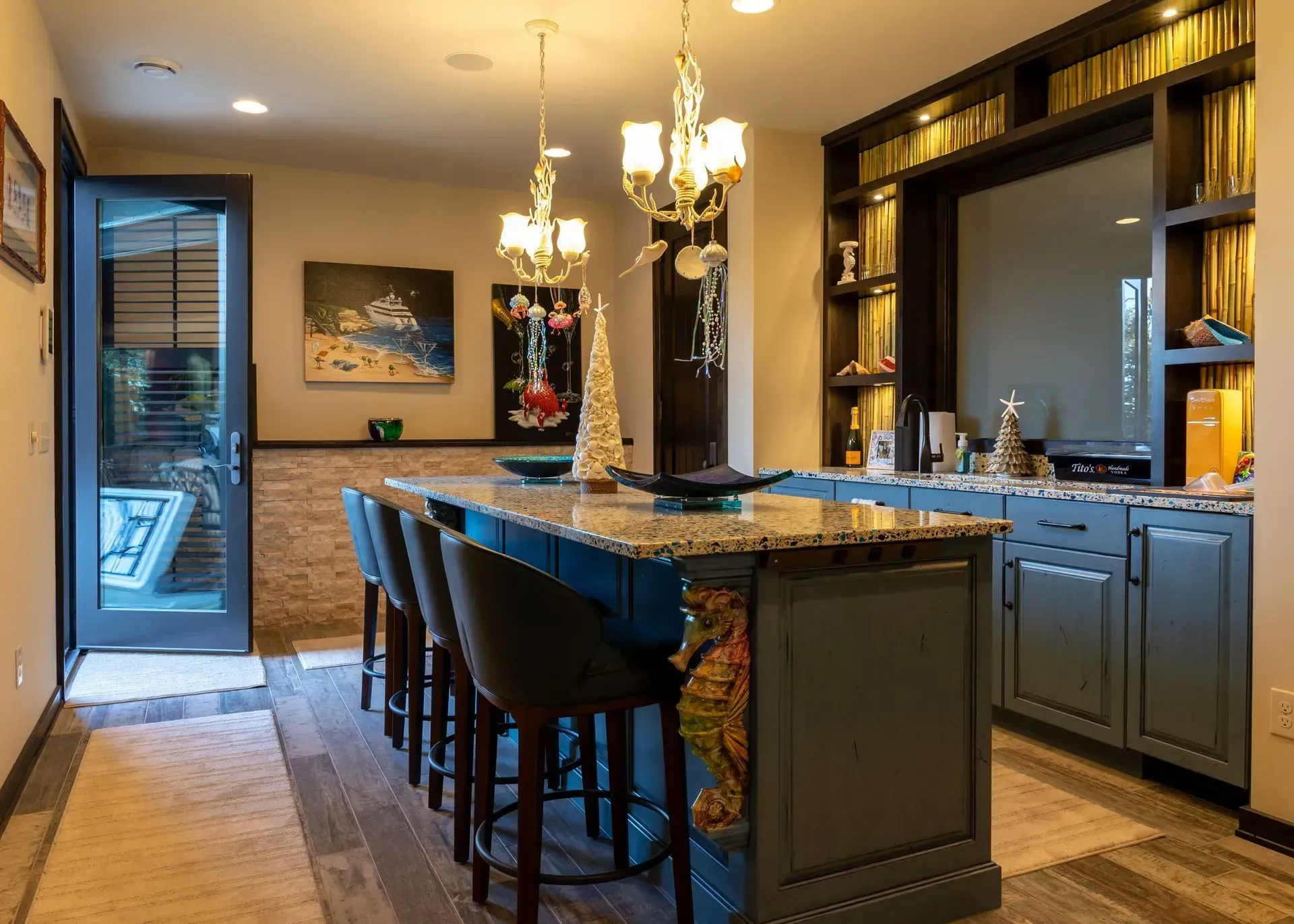 Blue bar with stools, chandeliers, artwork, and open doorway in a warmly lit room.