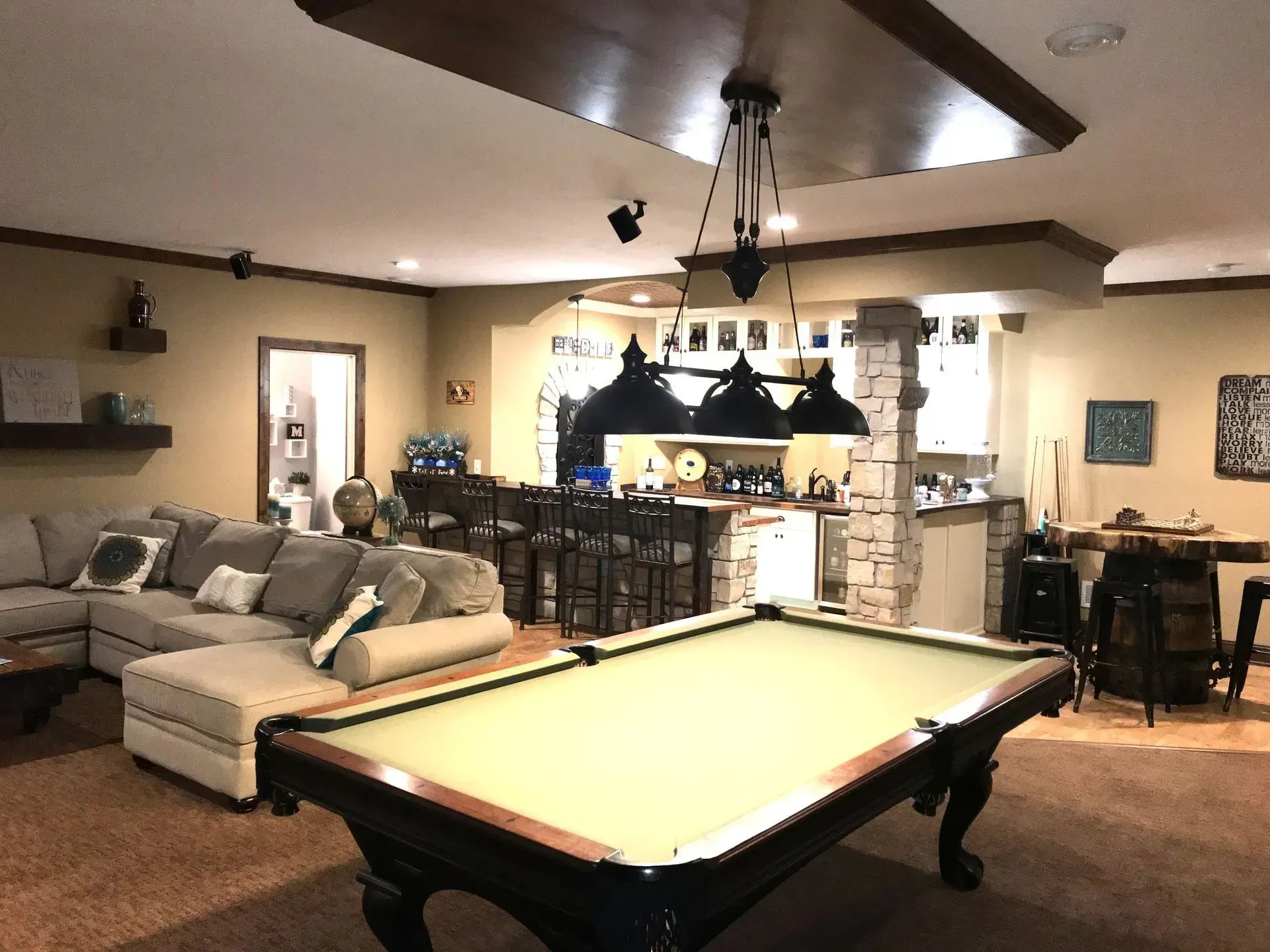 Pool table in a finished basement, with a bar, sofa, and overhead lighting.