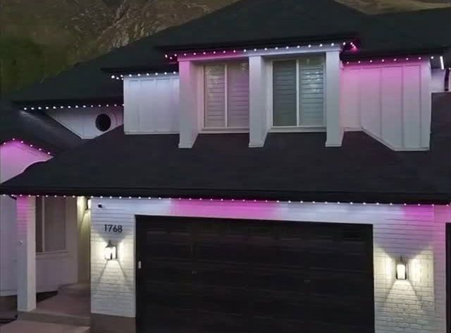 Two-story house at dusk with pink and white holiday lights along the roofline and garage