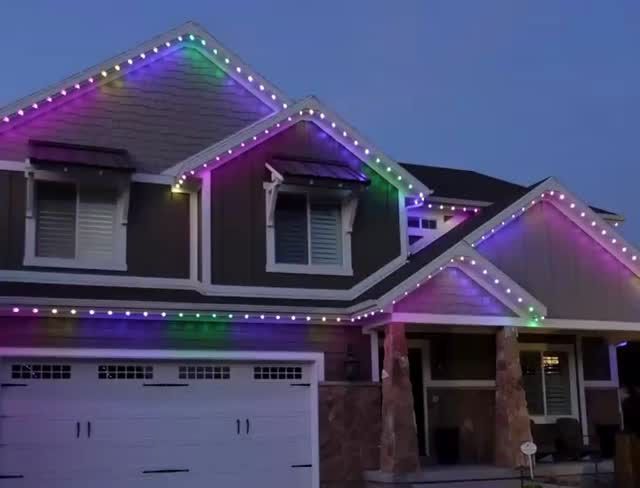 Suburban house with colorful string lights outlining the roof at dusk