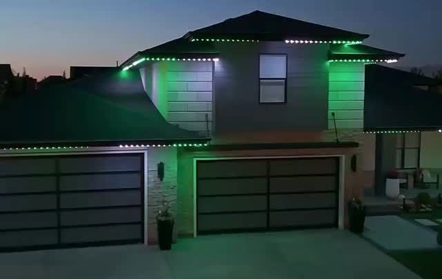 Two-story suburban house at dusk with green accent lights and a three-car garage