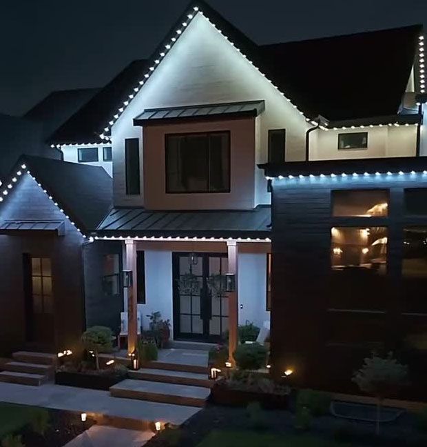 Modern two-story house at night with white roofline lights and lit windows