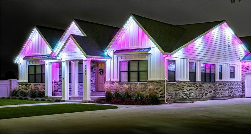 House with colorful pink and purple holiday lights lit along the roof at night