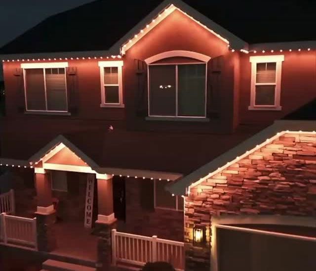 House outlined with warm white string lights at night, showing a festive front porch and roofline.