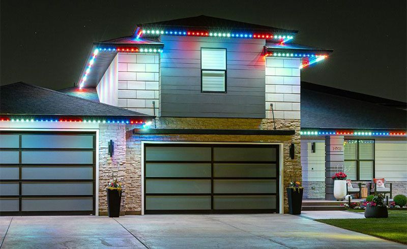 Modern two-story house with colorful Christmas lights outlining the roof and garage at dusk