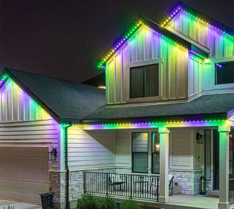 Two-story suburban house with multicolored holiday lights along the roofline at night