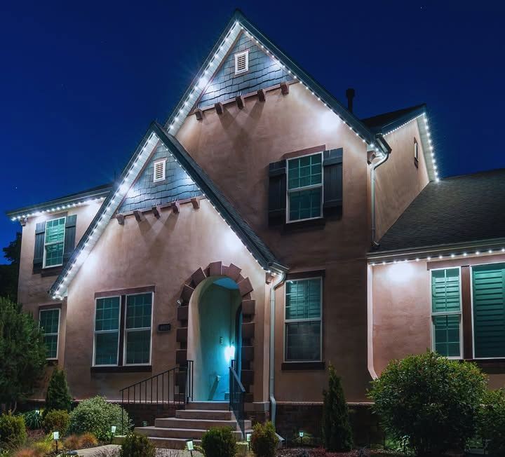 Two-story house at night with white roof lights, teal door glow, and landscaped front yard