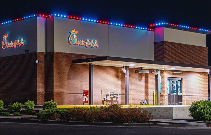 A Chick-fil-A restaurant at night with red and blue roof lights and a lit drive-thru entrance.