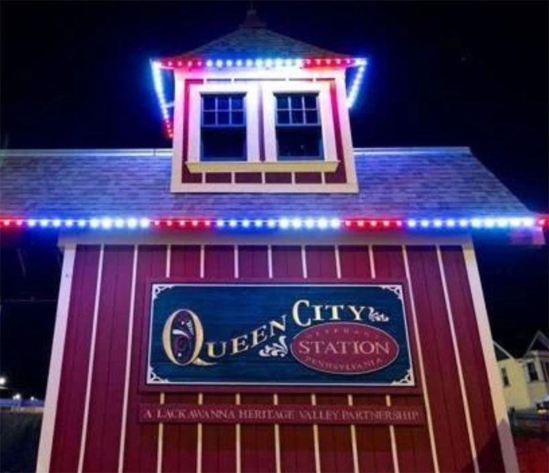 Night-lit red building with blue-white trim and a sign reading “Queen City Station”