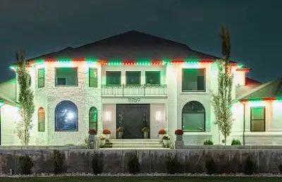Large white two-story house lit at night with colorful roof lights and arched windows