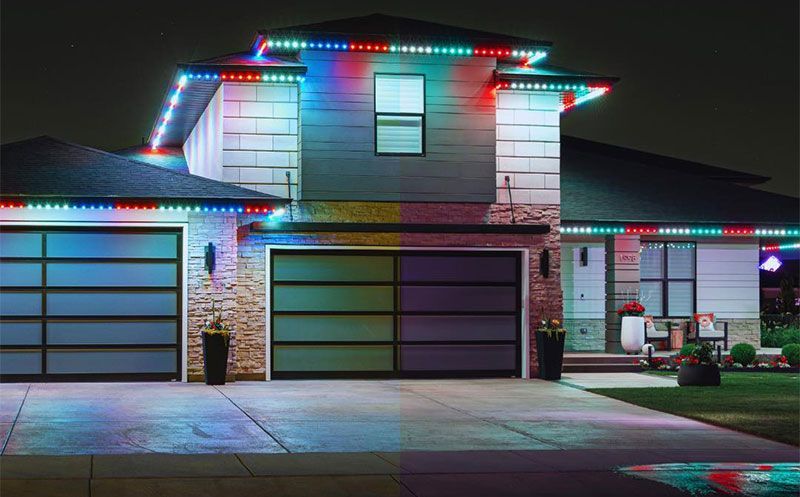 Suburban house at night outlined with red and blue holiday lights, two garages and front entrance visible