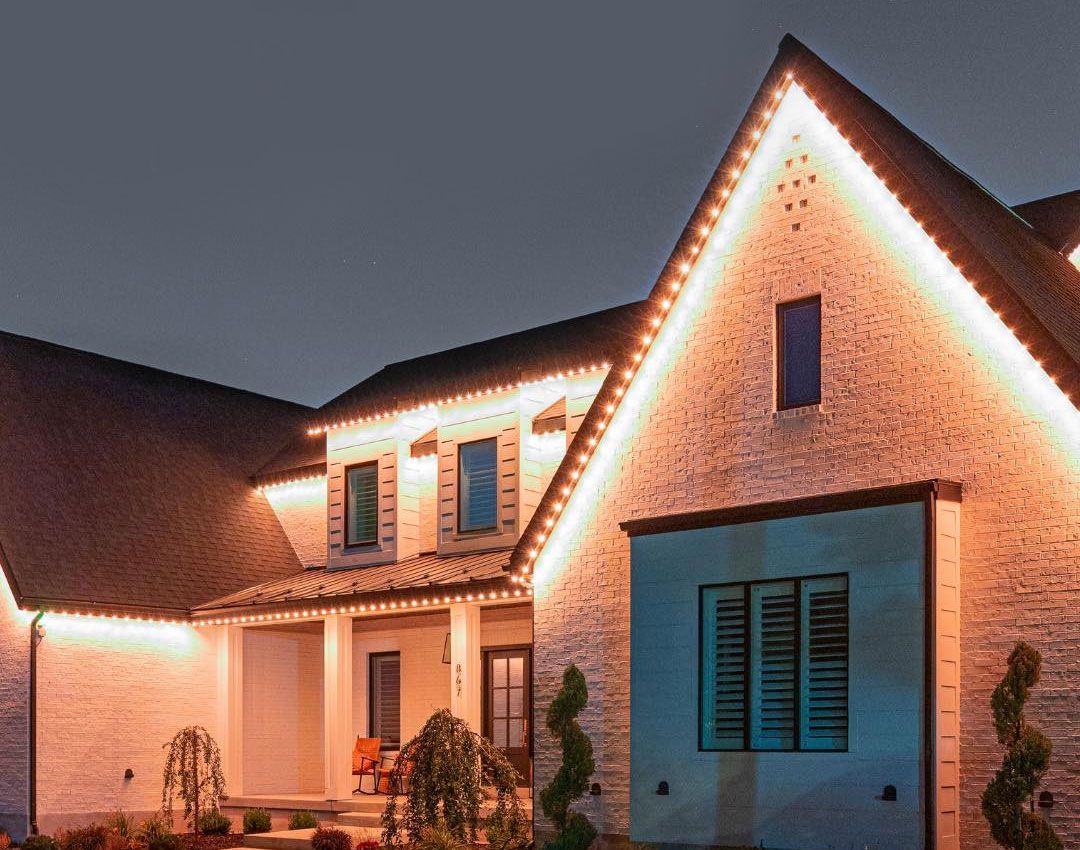 Modern house exterior at dusk with warm white roofline lights and blue garage doors
