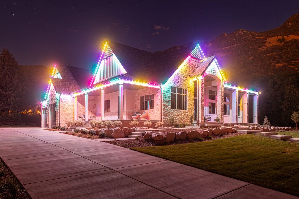 House decorated with colorful Christmas lights at night, viewed from a driveway.