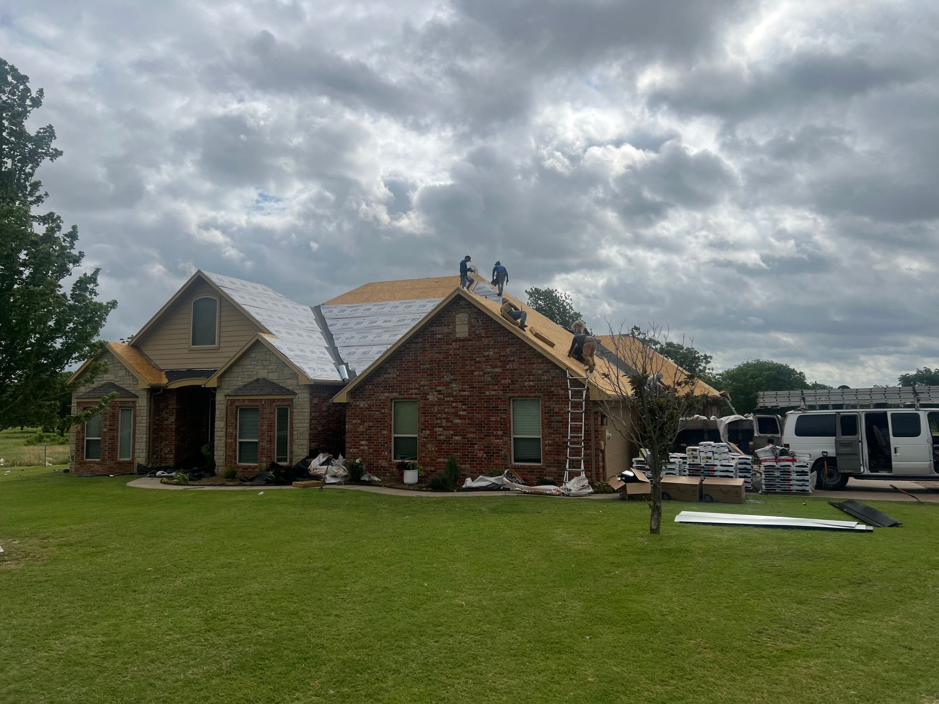 Roofers working on a residential home with brick and stone, cloudy sky.