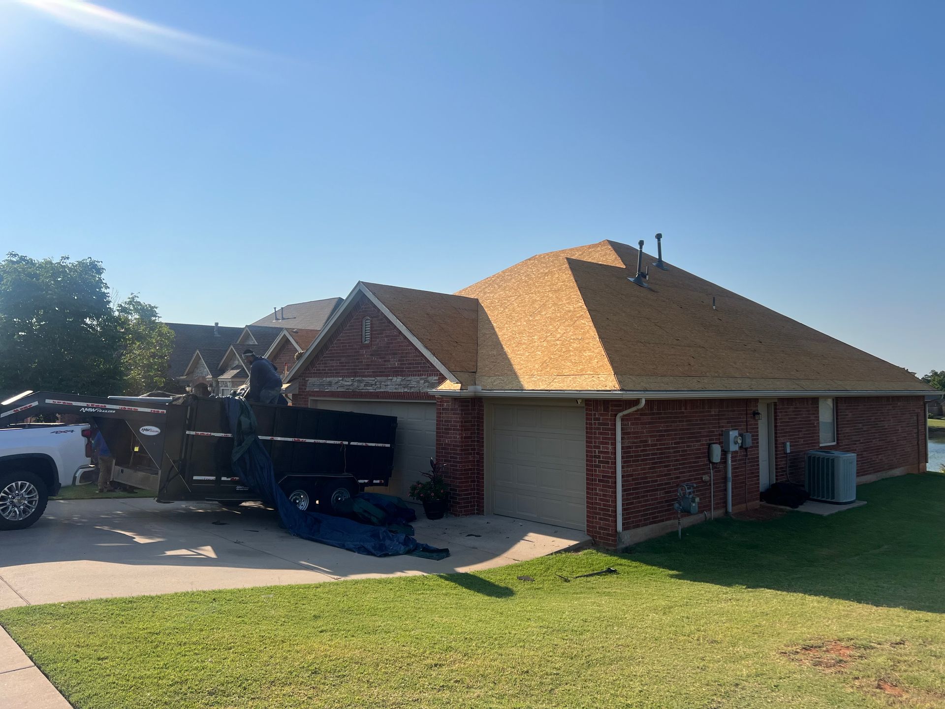 A house with new roofing, construction materials in front of a garage, and a truck parked nearby.