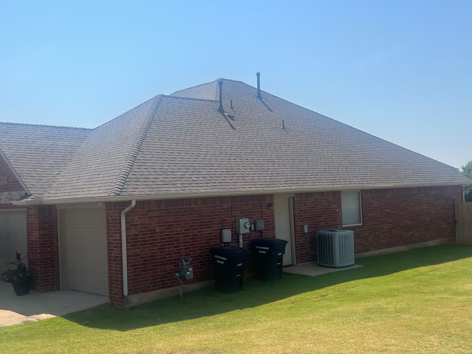 Brick house with a dark roof and green lawn on a sunny day.