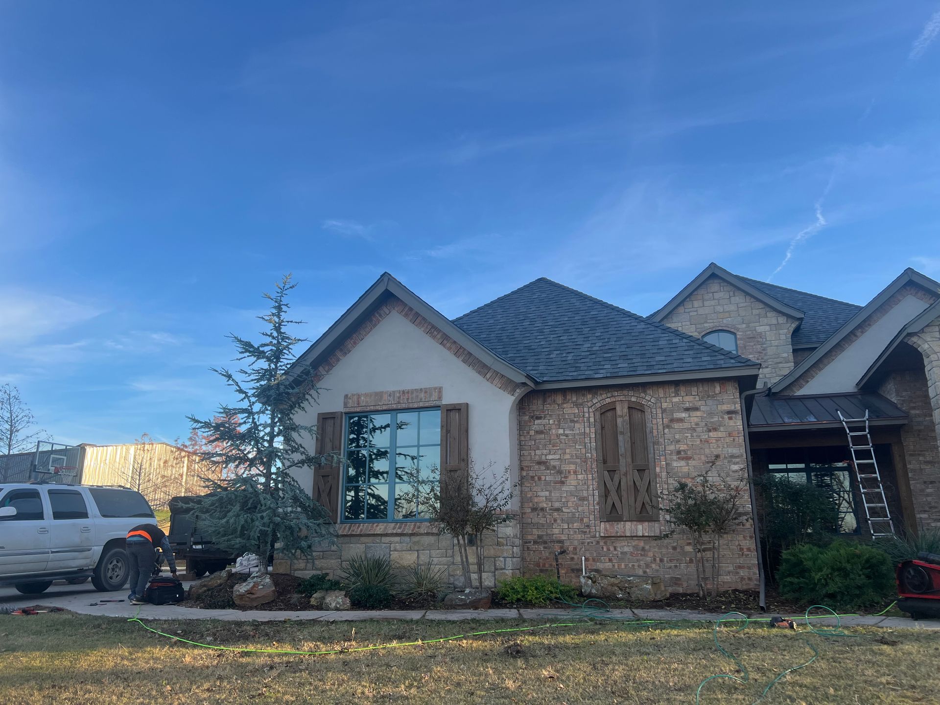 A house with a brick facade and dark roof under a blue sky, a truck parked nearby.