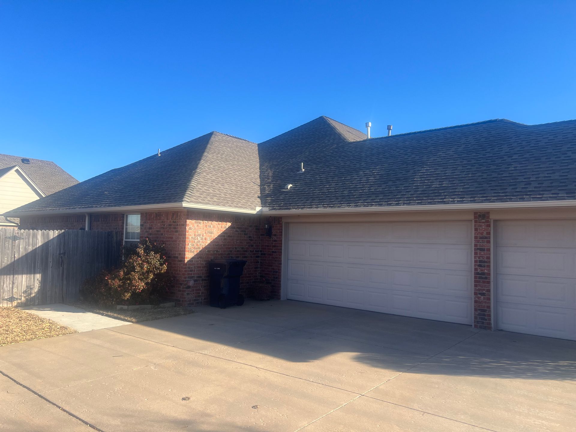 Brick townhome with two garage doors and a dark gray roof under a clear blue sky.