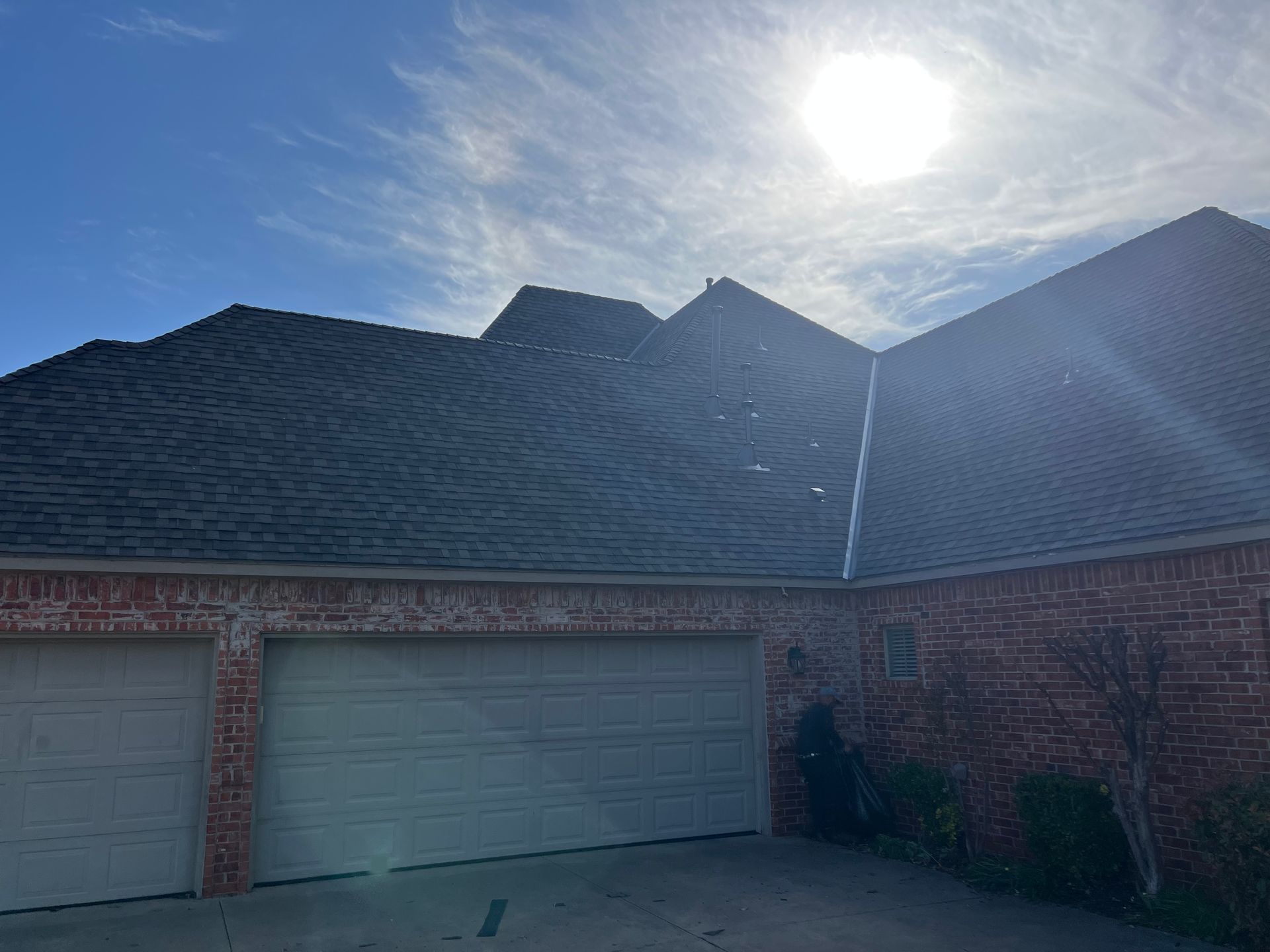 Garage with gray roof under a bright sun, set against a blue, cloudy sky.