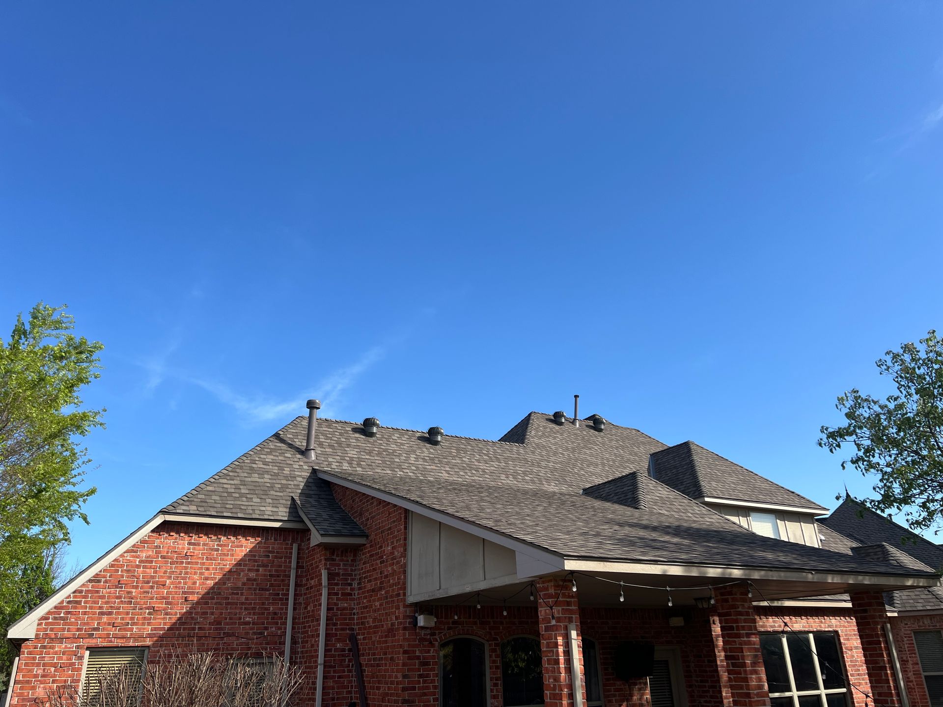 Brick house exterior with shingled roof, blue sky backdrop.