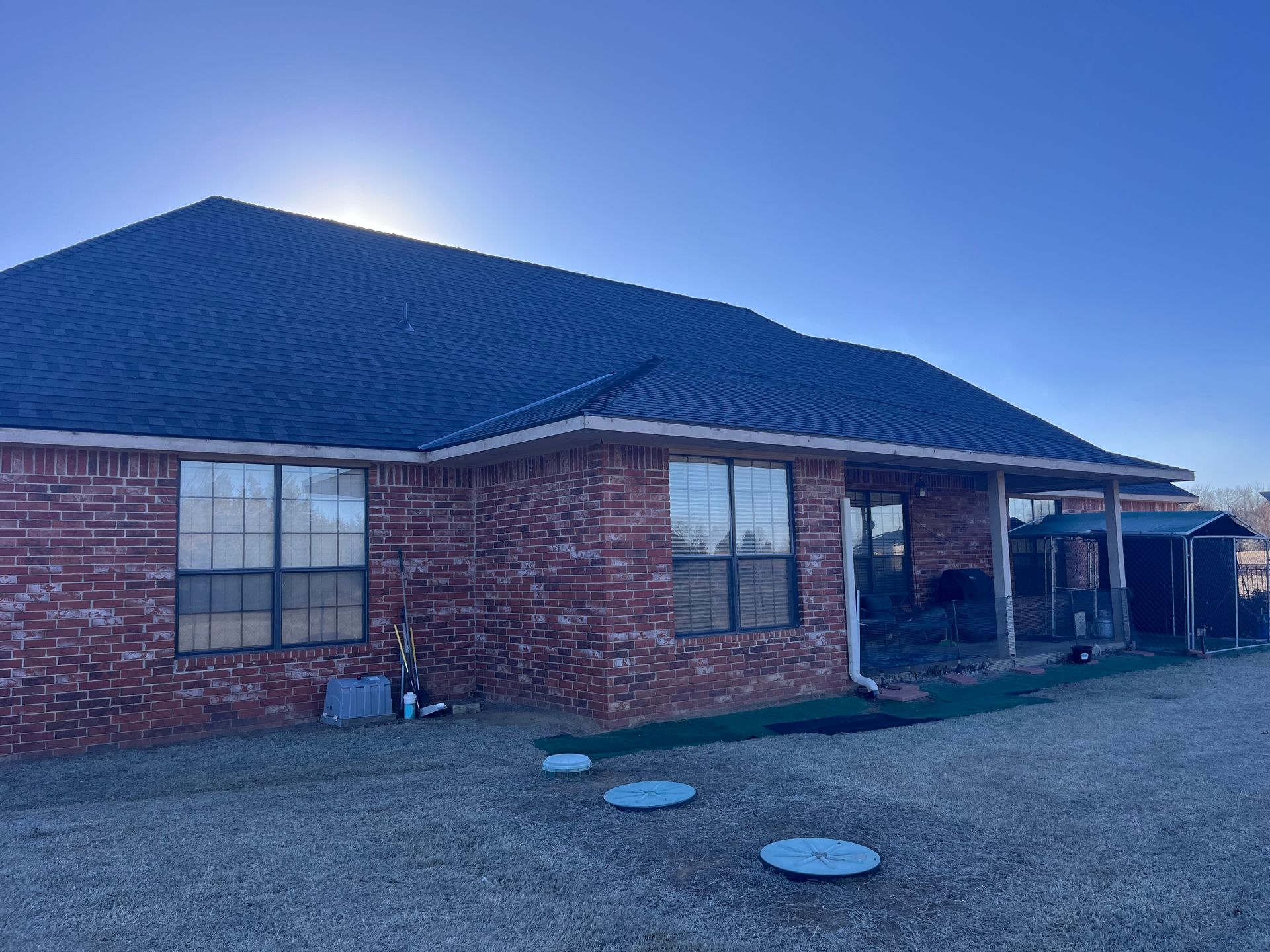 Red brick house with a dark roof and a covered patio on a sunny day.