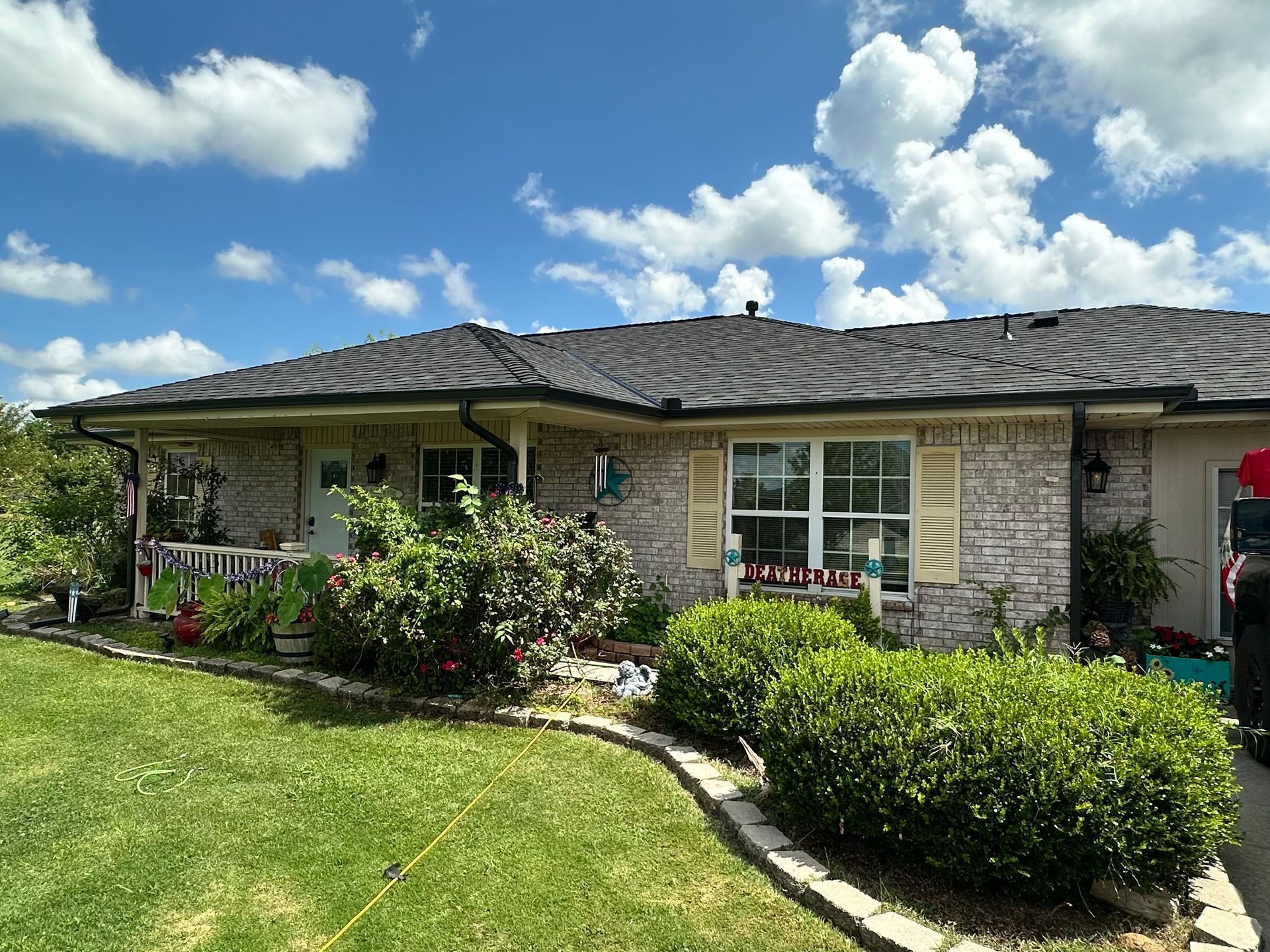 House with brick facade, lush green landscaping, and blue sky with puffy clouds.