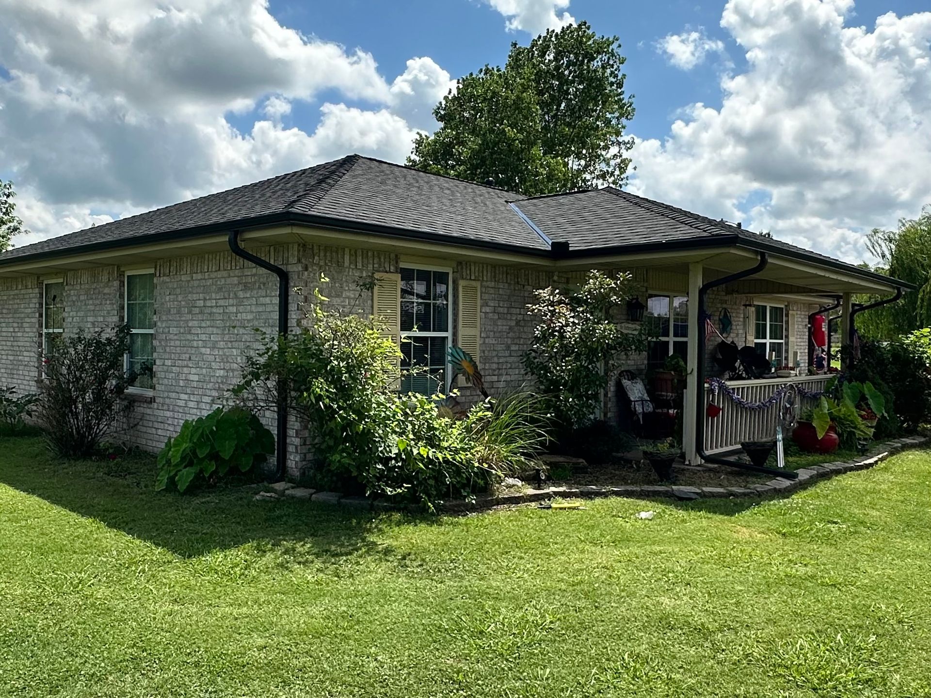 A brick house with a dark roof and green lawn on a sunny day.