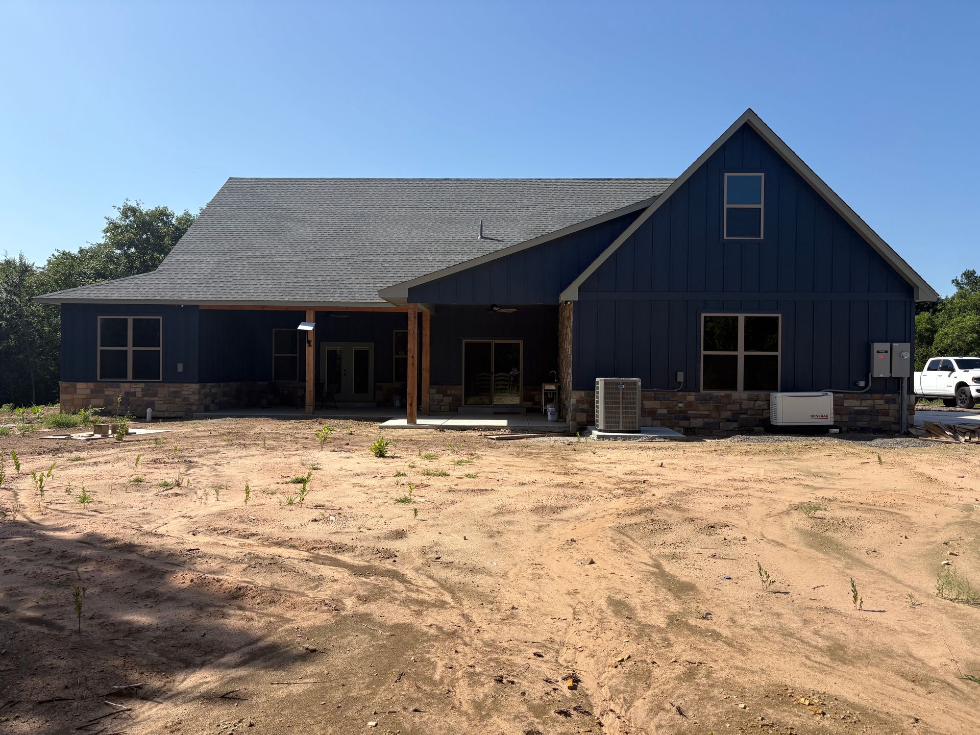 Blue house with stone base and covered patio on a sandy lot under a blue sky.