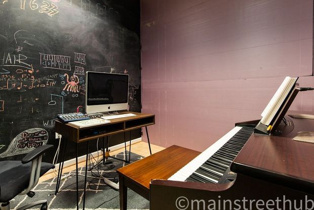A music studio with a piano, computer, desk, and chalkboard wall.