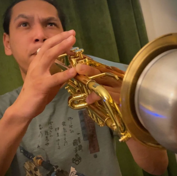 Person playing a gold trumpet, looking upward, indoors.