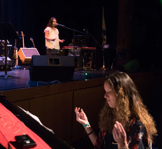 Woman at piano, with a musician singing on stage, concert setting.