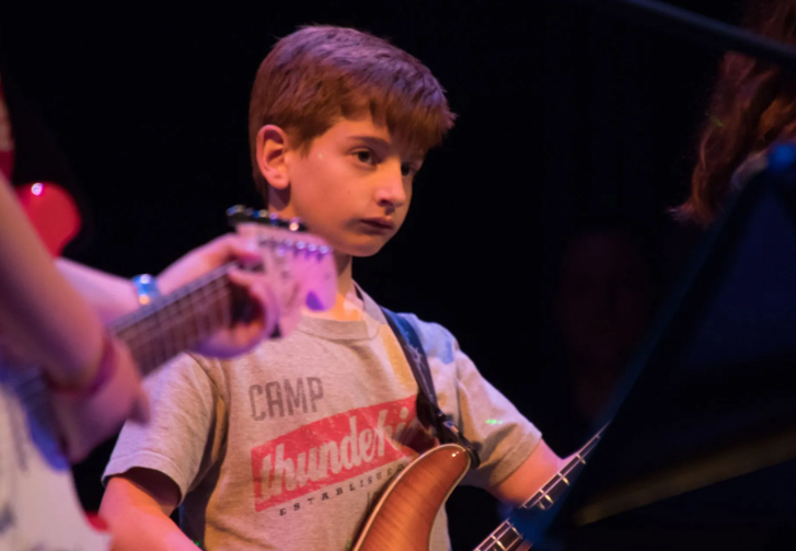 Boy playing bass guitar on stage, wearing a gray t-shirt.