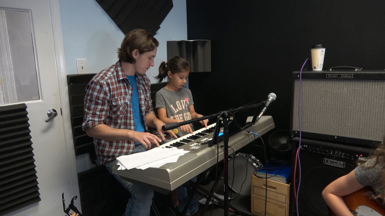 A man and a child playing a keyboard together in a music studio, sheet music on stand.