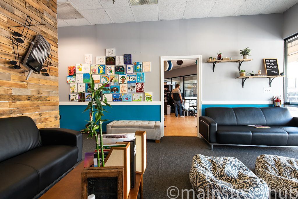 Cozy waiting room with black couches, wall art, and a doorway leading to another room.
