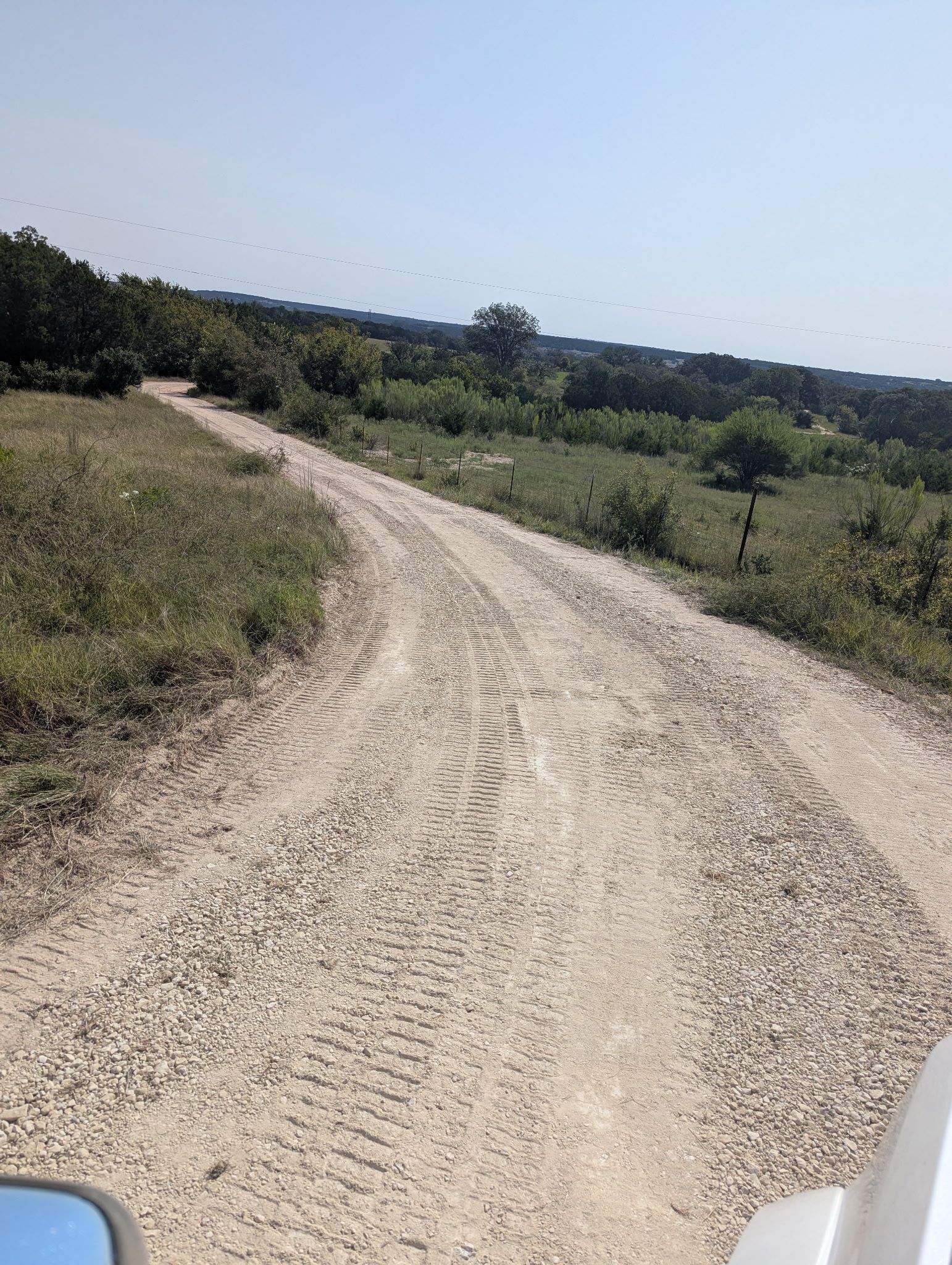 Dirt road winding through a grassy landscape under a clear sky.