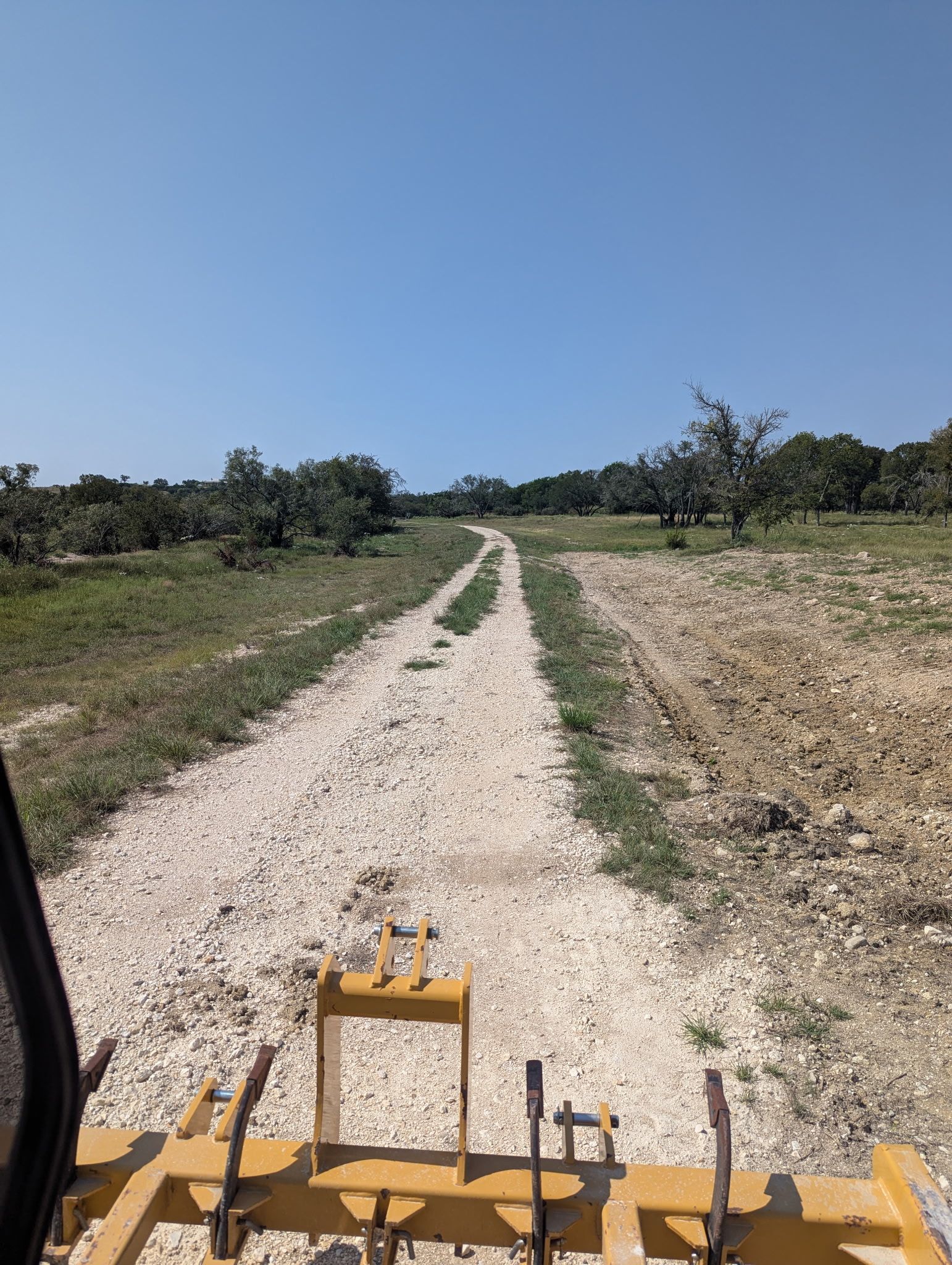 Gravel road through a field under a blue sky, seen from the seat of a tractor.
