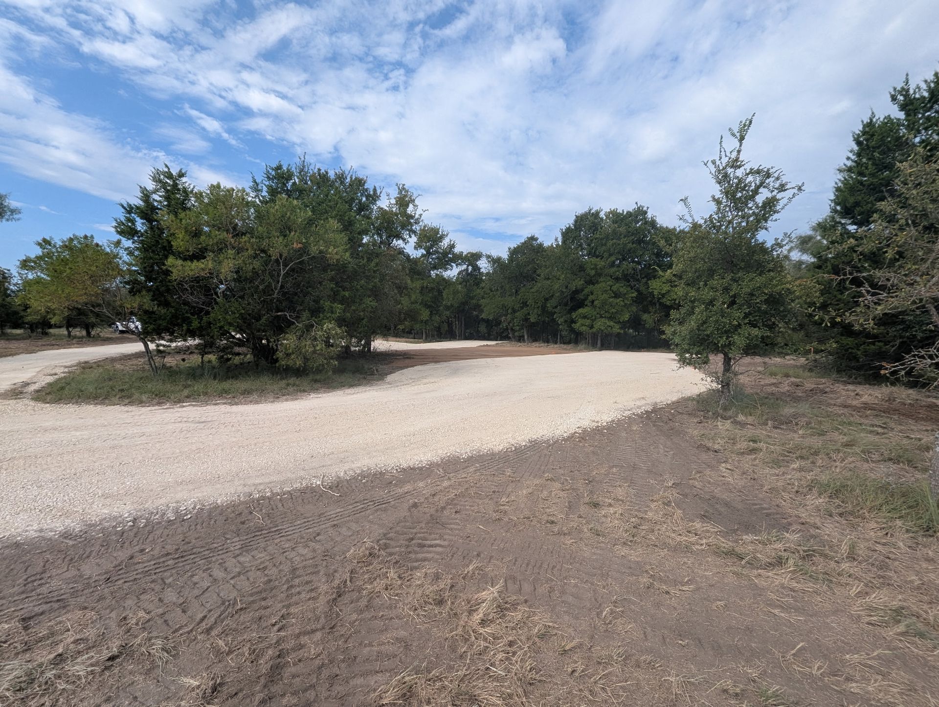 Gravel road curving through trees under a partly cloudy blue sky.
