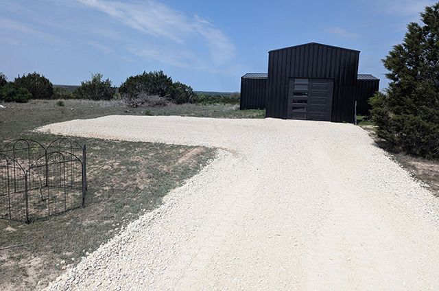 A gravel driveway leading to a black building in the middle of a field
