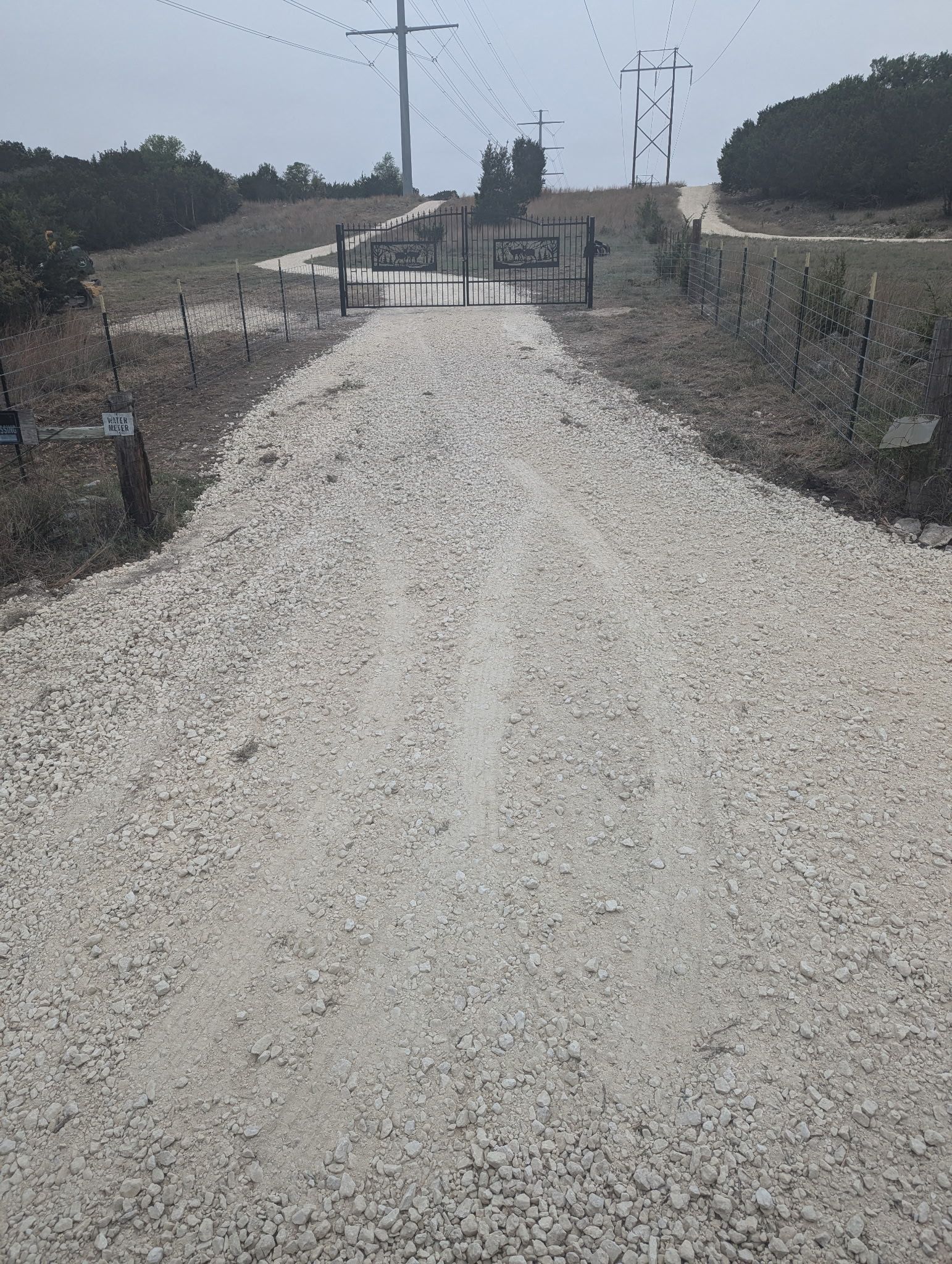 A gravel road going through a field with a gate in the middle