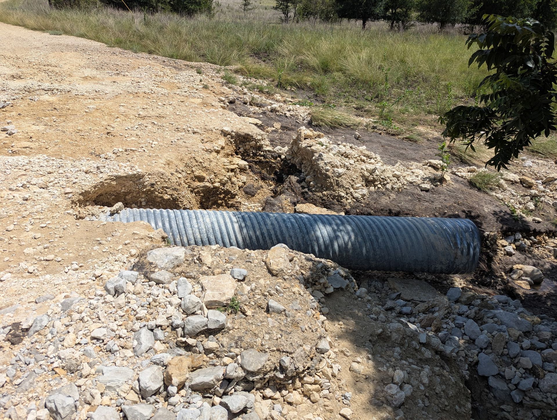 A large pipe is laying in the dirt next to a stream