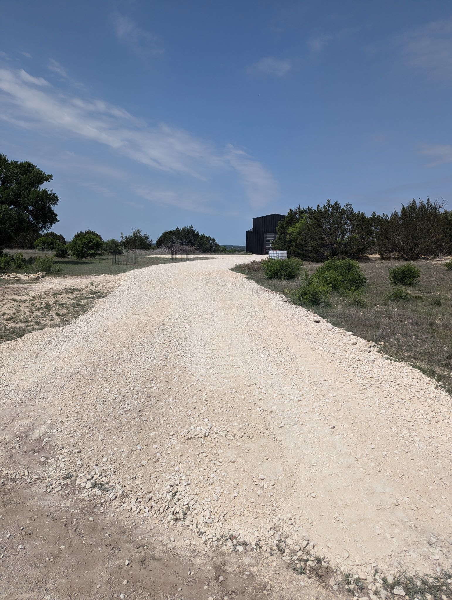 A gravel road going through a field with trees on both sides