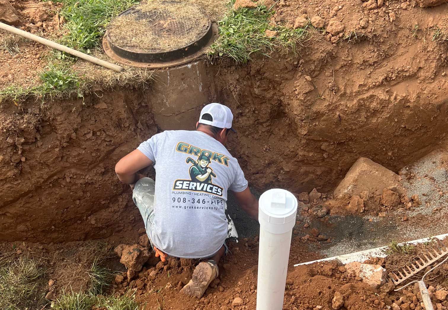 a man in a gray shirt works on a septic system in a ditch