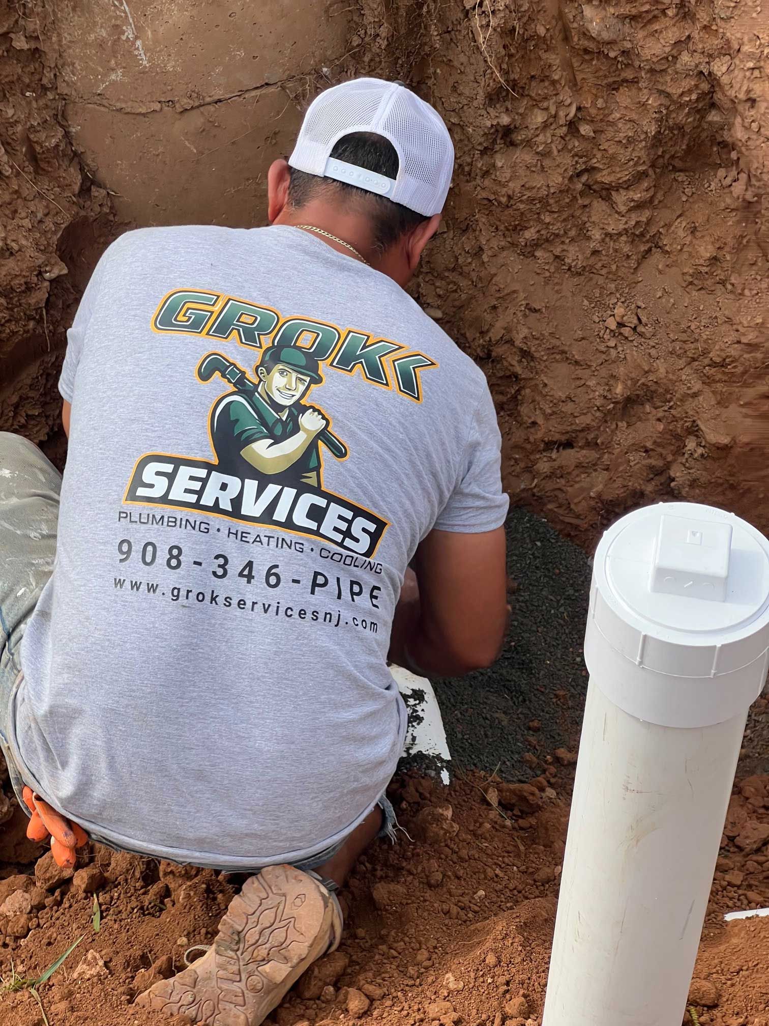 plumber working in a trench, wearing a gray shirt with company logo
