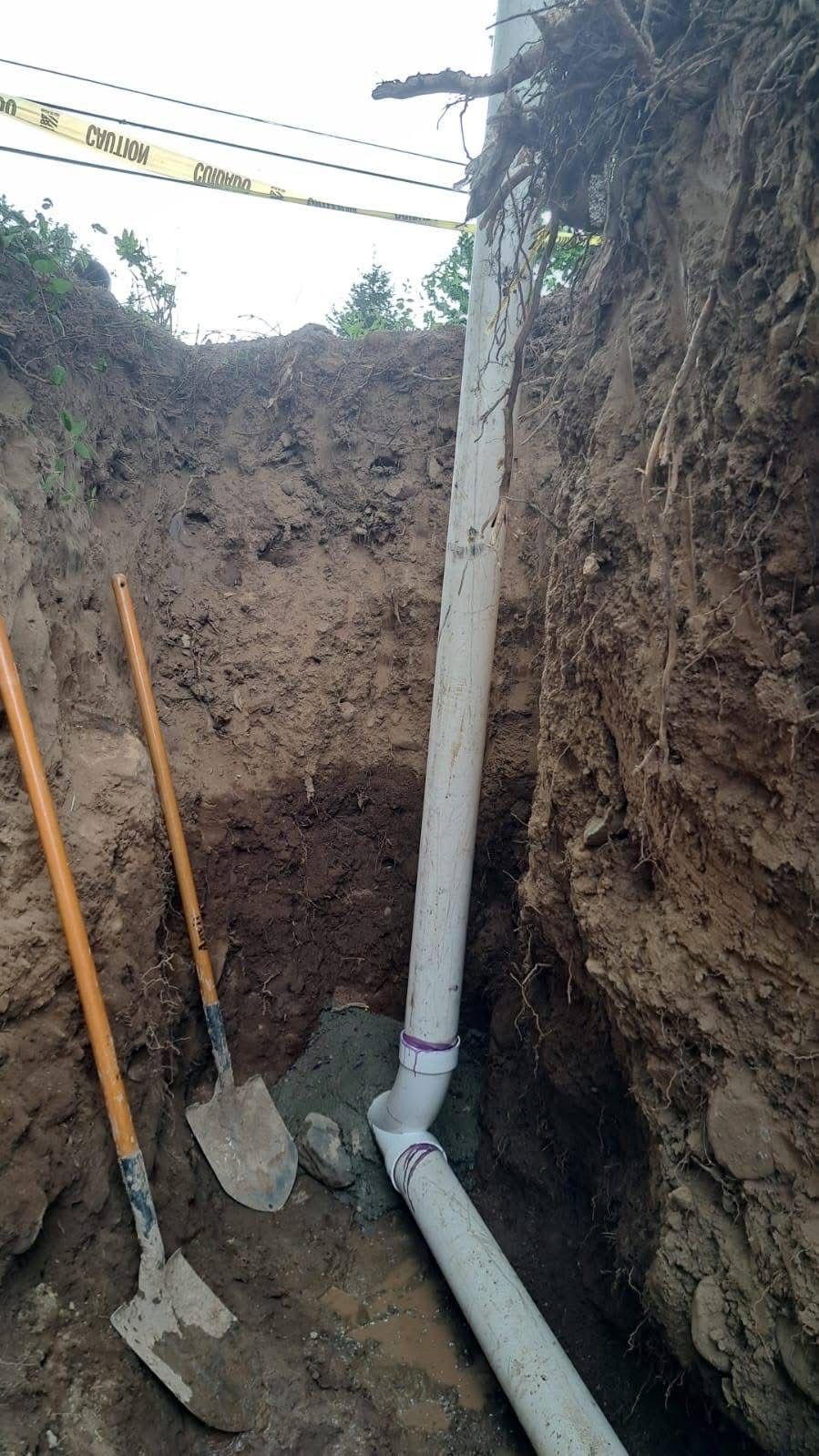 a trench with white PVC pipes, two shovels rest beside the trench