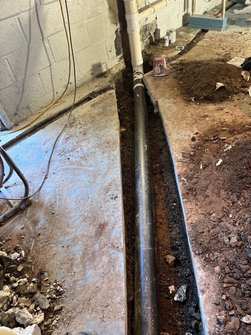 basement trench with black pipe, dirt, concrete floor, and white wall