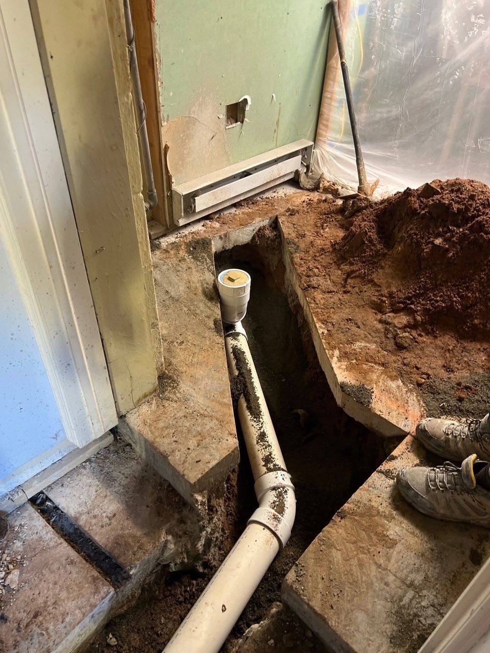 a trench dug in a room exposes white PVC pipes, a wall heater, and a doorway