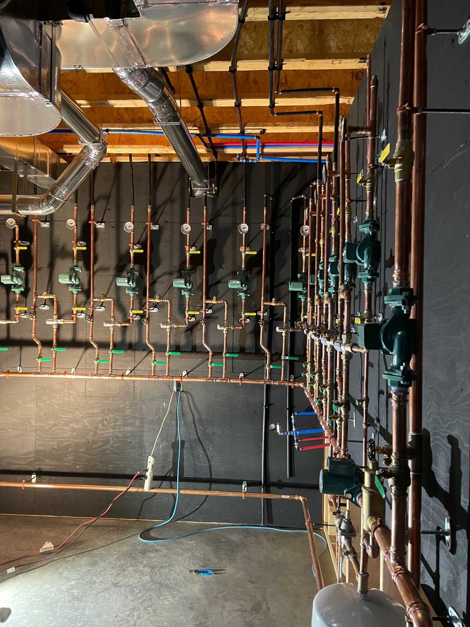 copper pipes and mechanical equipment mounted on a black wall in an industrial setting