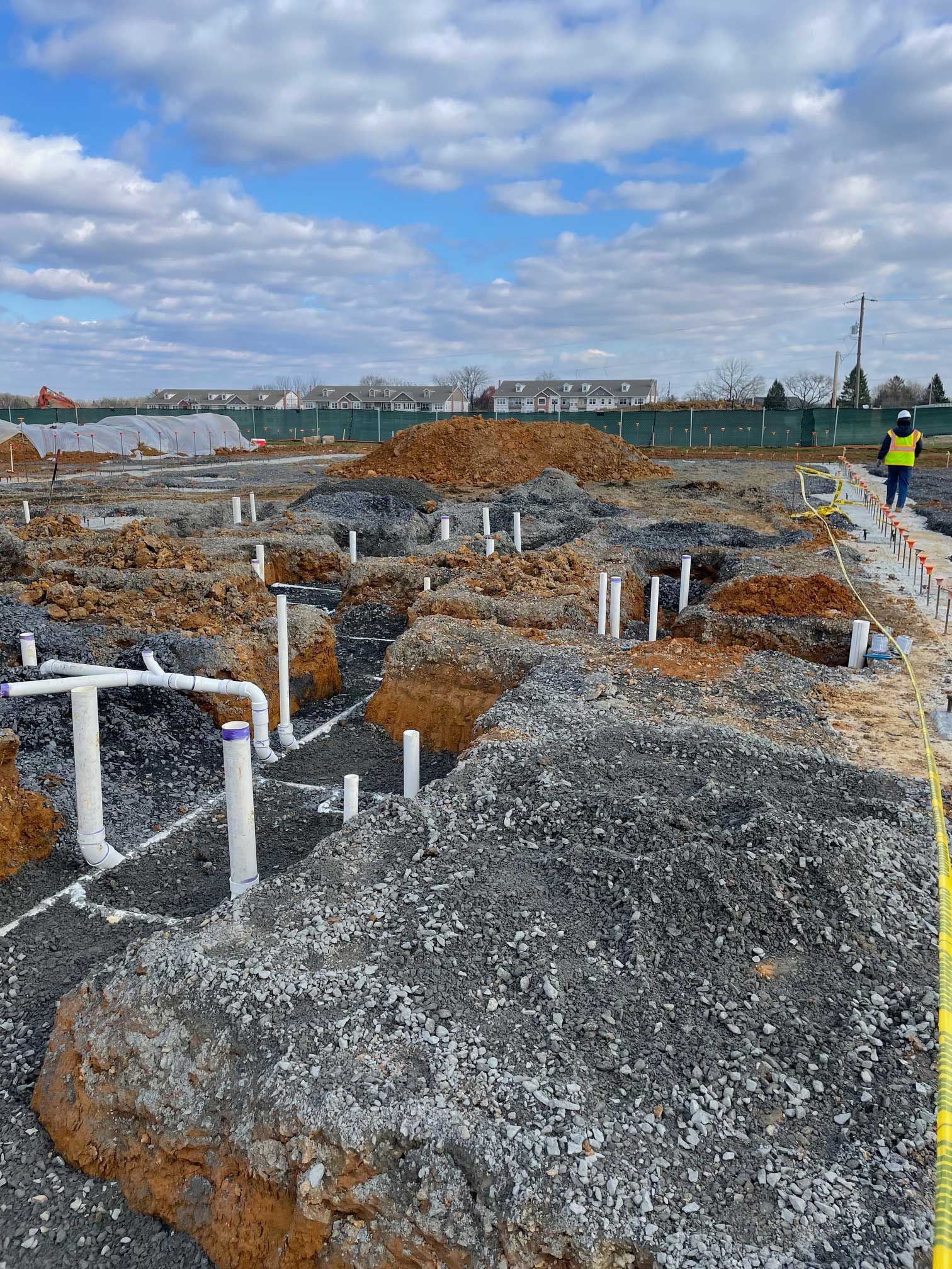 construction site with white PVC pipes, dirt piles, and a worker in a yellow vest