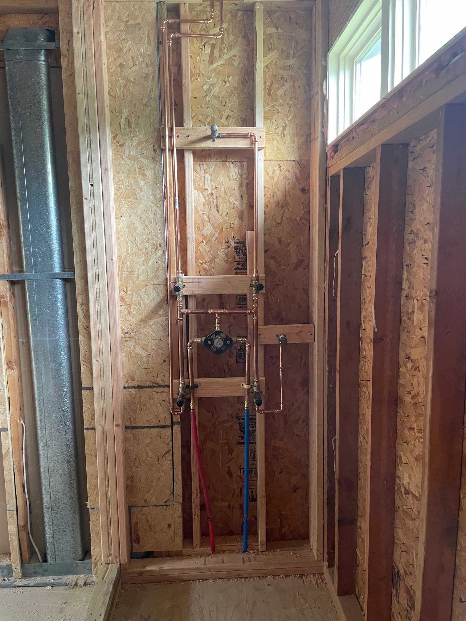 copper plumbing pipes within wooden framing for a shower, red/blue water lines, unfinished construction